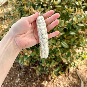 May include: A white crocheted keychain with a silver loop. The keychain is made of small, round stitches and is about 5 inches long.