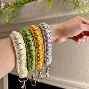 May include: Four crocheted keychains in different colors: cream, green, yellow, and gray. Each keychain has a silver metal clasp.
