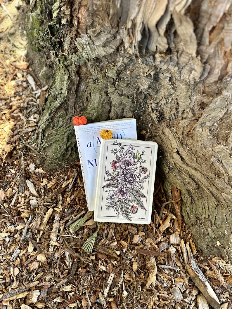 May include: Two books with floral designs and crocheted bookmarks. The book on top has the text "A Mind" and "NU" visible. The book on the bottom has a floral design with a fern and anemone.
