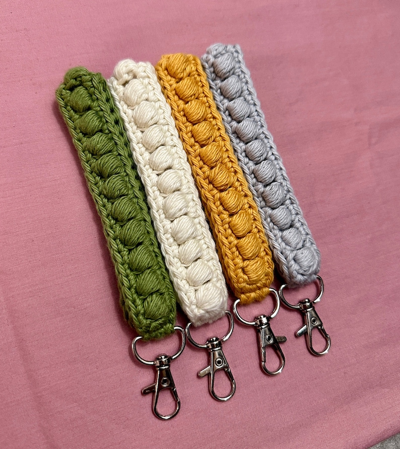 May include: Four crocheted keychains in green, white, yellow, and gray with silver key rings.