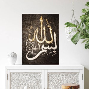 May include: Textured black wall art featuring gold and white Arabic calligraphy. The artwork displays the word "Allah" in a stylized script, with gold leaf accents. The piece is displayed on a white cabinet.