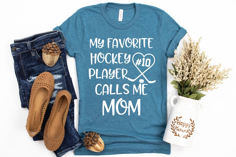 May include: A teal blue t-shirt with the text "My favorite hockey player #10 calls me mom" in white. The text is surrounded by a heart and hockey sticks.