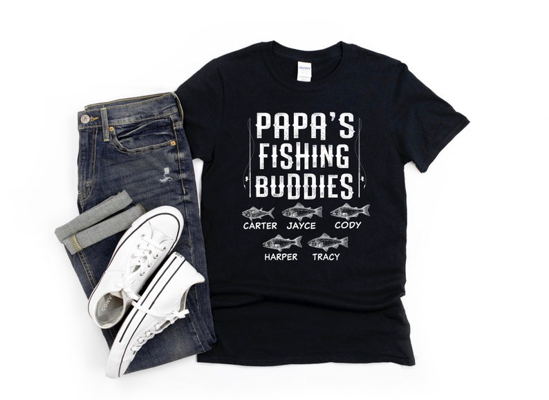 Puede incluir: Camiseta negra con texto blanco que dice "Papa's Fishing Buddies" con un gr&aacute;fico de ca&ntilde;a de pescar y cinco peces con nombres debajo de cada pez: Carter, Jayce, Cody, Harper y Tracy.