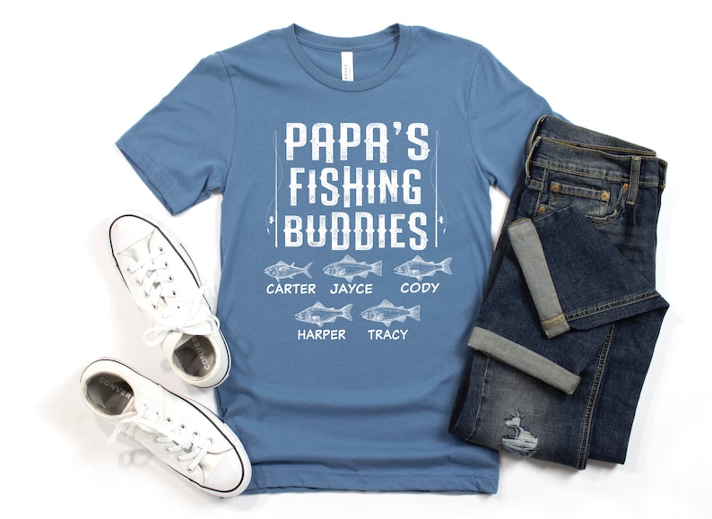 Puede incluir: Una camiseta azul con el texto "Papa's Fishing Buddies" y los nombres Carter, Jayce, Cody, Harper y Tracy impresos debajo. Cada nombre est&aacute; emparejado con una ilustraci&oacute;n de un pez.