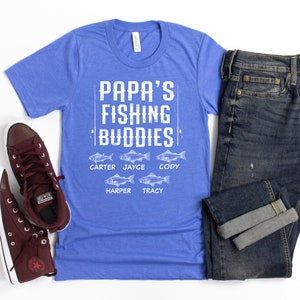 Puede incluir: Una camiseta azul con el texto "Papa's Fishing Buddies" y los nombres Carter, Jayce, Cody, Harper y Tracy impresos debajo. Los nombres est&aacute;n emparejados con un peque&ntilde;o gr&aacute;fico de pescado.