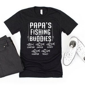 Puede incluir: Camiseta negra con texto blanco que dice "Papa's Fishing Buddies" y enumera los nombres "Carter, Jayce, Cody, Harper, Tracy" con un gr&aacute;fico de pescado al lado de cada nombre.