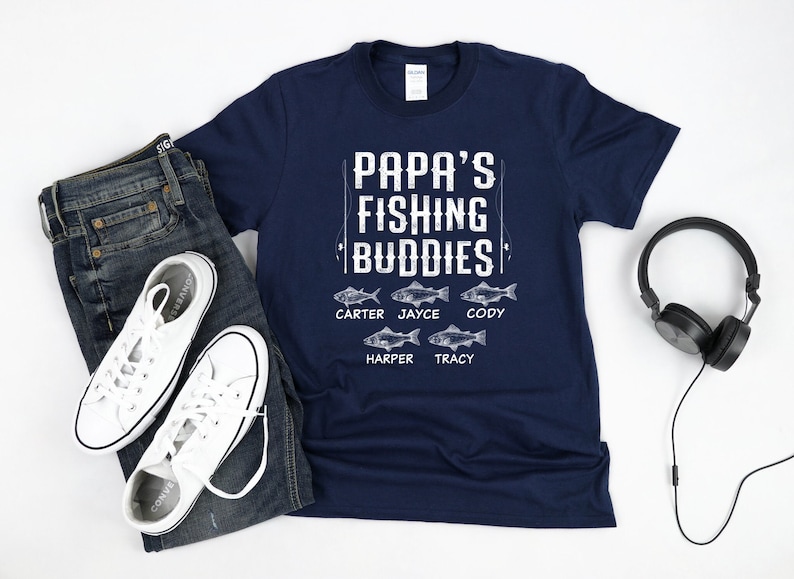 Puede incluir: Una camiseta azul marino con el texto "Papa's Fishing Buddies" y un gr&aacute;fico de cinco peces con nombres debajo de cada pez: Carter, Jayce, Cody, Harper y Tracy.