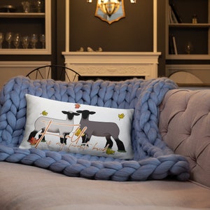 Può includere: Cuscino bianco con una grafica di due pecore con la faccia nera con foglie autunnali e il testo "Faith is my favorite breed".