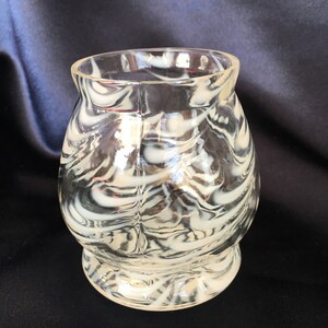 May include: A clear glass vase with a swirling black and white pattern. The vase has a rounded body and a flared lip.