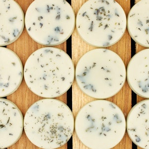 May include: Ten round, white, scented wax melts with green flecks, arranged in two rows of five on a wooden surface.