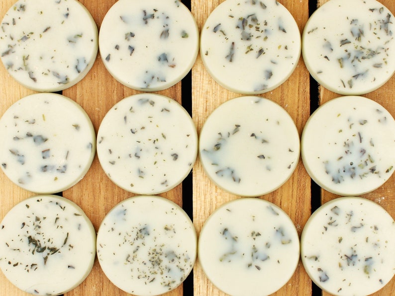May include: Ten round, white, scented wax melts with green flecks, arranged in two rows of five on a wooden surface.