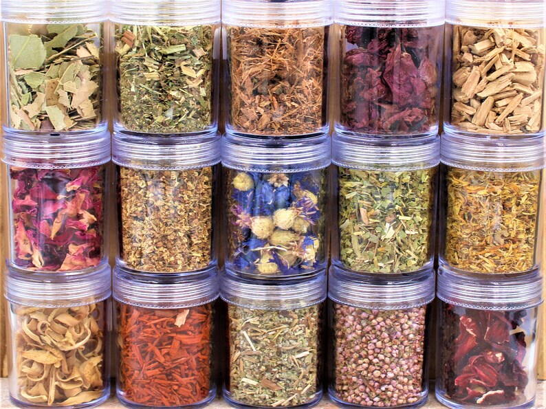 May include: Twenty clear glass jars filled with various dried herbs and flowers. The jars are arranged in three rows of six jars each. The herbs and flowers are a variety of colors, including red, pink, yellow, green, and brown.