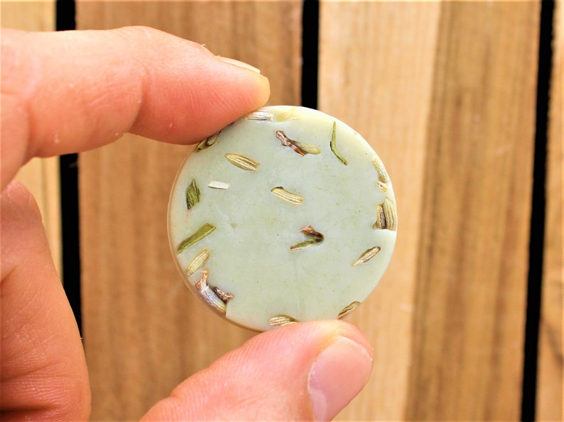 May include: A round, light green soap bar with dried herbs and flowers embedded in it.