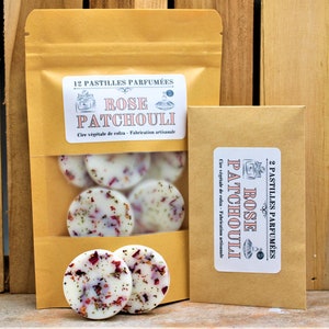 Peut inclure: Deux sachets en papier kraft avec des étiquettes indiquant "12 Pastilles Parfumées Rose Patchouli" et "2 Pastilles Parfumées Rose Patchouli". Les sachets contiennent des pastilles de cire blanche avec des pétales de rose séchés.