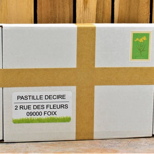 May include: A white cardboard box with brown tape and a label that reads "PASTILLE DECIRE 2 RUE DES FLEURS 09000 FOIX".