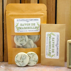 Peut inclure: Deux petits sachets de cire parfumée avec une barre de savon à l'huile d'olive. Les sachets sont bruns et portent des étiquettes blanches avec des branches d'olivier vertes et le texte "Savon de Marseille" en français. La barre de savon est verte et porte le texte "Savon de Marseille" en français.