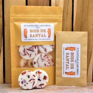 Könnte beinhalten: Zwei braune Papiertüten mit Etiketten, auf denen "12 Pastilles Parfumées Bois de Santal" und "2 Pastilles Parfumées Bois de Santal" steht. Die Tüten enthalten weiße Wachs-Schmelzen mit roten Flecken.