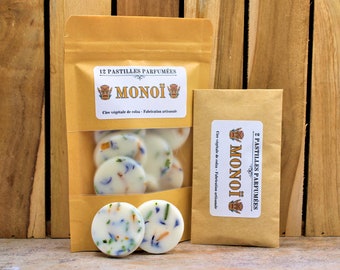 Puede incluir: Dos bolsas de papel marrón con etiquetas blancas. Las etiquetas tienen el texto "12 PASTILLES PARFUMÉES MONOI" y "2 PASTILLES PARFUMÉES MONOI" en texto negro. Las bolsas contienen pastillas de cera blanca con motas de colores.
