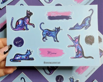 May include: A sheet of stickers featuring galaxy-themed cats with the word "Meow" written on them. The stickers are on a light blue background. The text "@innerwildernessart" is also included on the sheet.