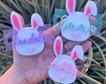 May include: Three white bunny-shaped acrylic keychains with glitter backgrounds. The keychains are personalized with the names "Kendall", "Emma", and "Ashley".