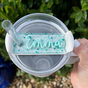 May include: White tumbler with a clear lid and a turquoise glitter name tag that says "Emma".