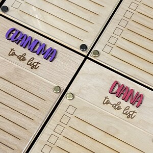 Pode incluir: Dois quadros de madeira de lista de tarefas pendentes com uma sobreposi&ccedil;&atilde;o de acr&iacute;lico transparente. O quadro superior tem o texto "GRANDMA to-do list" em letras roxas. O quadro inferior tem o texto "DIANA to-do list" em letras vermelhas.