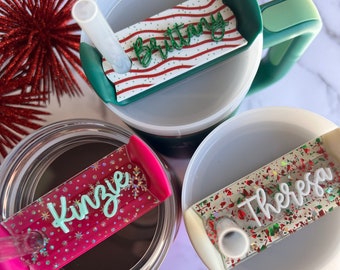 May include: Three personalised Christmas-themed tumbler lids with names "Brittany", "Kinzie", and "Theresa" in glitter lettering. Each lid has a different design with red and green colours.