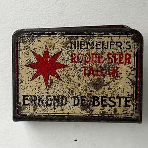 May include: Rectangular, vintage tobacco tin with a distressed, speckled finish. The tin features a red starburst design and text in black and red, including "NIEMEIJER'S ROODE STER TABAK" and "ERKEND DE BESTE".
