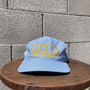 May include: A light blue baseball cap with a yellow embroidered logo that reads "UCLA University of California LA".