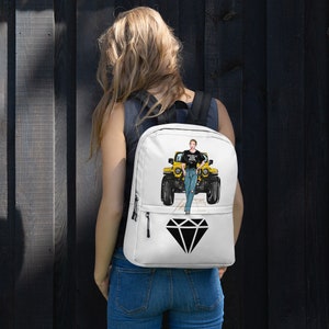 May include: White backpack with a graphic of a yellow Jeep and a woman in jeans. The backpack has a black diamond graphic and the text "Wheels & Heels". It has black straps and zippers.