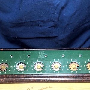 May include: Vintage Lightning Adding Machine Co. calculator with a green face and brown frame. The calculator has several number dials and the text "The Lightning Adding Machine Co. Los Angeles Calif. U.S.A."