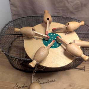 May include: A vintage wooden game with a circular base and five wooden pieces with red accents. The game is set inside a wire basket on a wooden surface. The game's design is simple and classic.