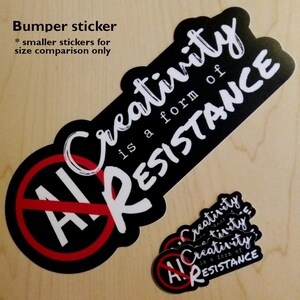 May include: Black bumper sticker with the text "Creativity is a form of RESISTANCE" in white script. The sticker also features a red circle with a line through the words "AI" in white. Smaller stickers with the same design are also present.