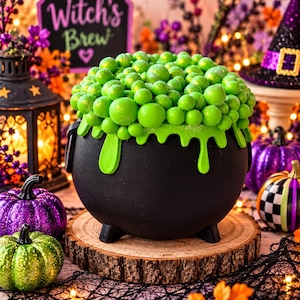 May include: A black cauldron-shaped cake featuring a vibrant green bubbling liquid effect on top, created with numerous small green spheres and dripping green icing along the rim, resting on a circular wooden base with a natural bark edge.