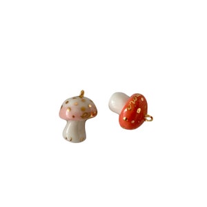 May include: Two ceramic mushroom charms with gold accents. One mushroom is pink and white with gold dots, the other is red with gold dots and the word "love" written in gold.