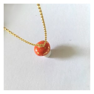 May include: A gold chain necklace with a red and white mushroom pendant. The mushroom has gold polka dots and the word "melt" written on it.