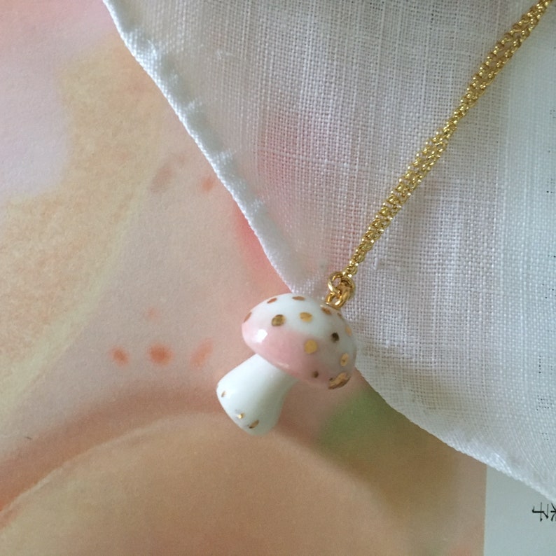May include: A delicate gold chain necklace with a pink and white porcelain mushroom pendant. The mushroom has gold speckles and a white stem.