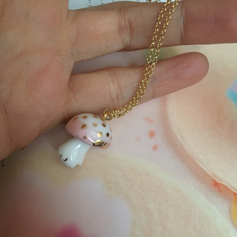 May include: A gold chain necklace with a pink and white porcelain mushroom pendant. The mushroom has gold dots and a white stem.