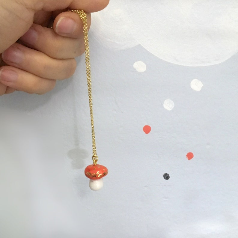 May include: A gold chain necklace with a red and white ceramic mushroom pendant.