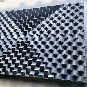 Pode incluir: Uma peça de arte de parede de madeira preta com um padrão geométrico de quadrados e retângulos. Os quadrados e retângulos são dispostos em um padrão escalonado, criando um efeito 3D.