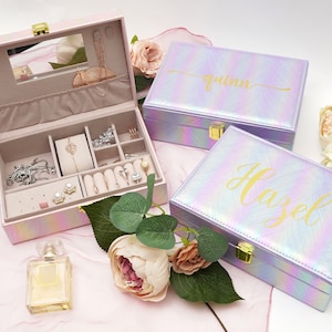 May include: Two iridescent pink and purple jewelry boxes with gold accents. The boxes have the names "Quinn" and "Hazel" written on them in gold lettering.