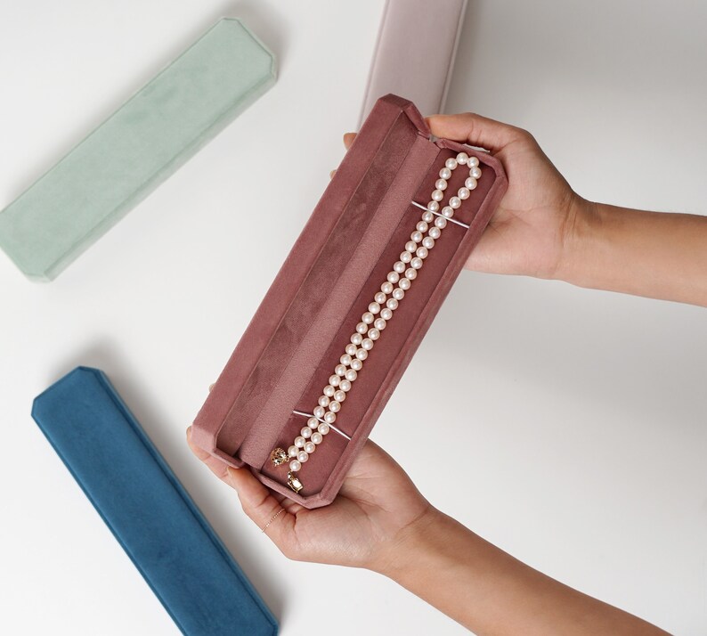May include: A pink velvet jewelry box with a pearl necklace inside. The box is open and the necklace is visible.