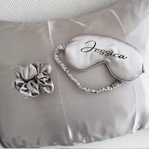 Może przedstawiać: Srebrna satynowa maska do spania z wyszytym imieniem "Jessica", srebrna satynowa opaska do włos&oacute;w i srebrna satynowa poszewka na poduszkę.