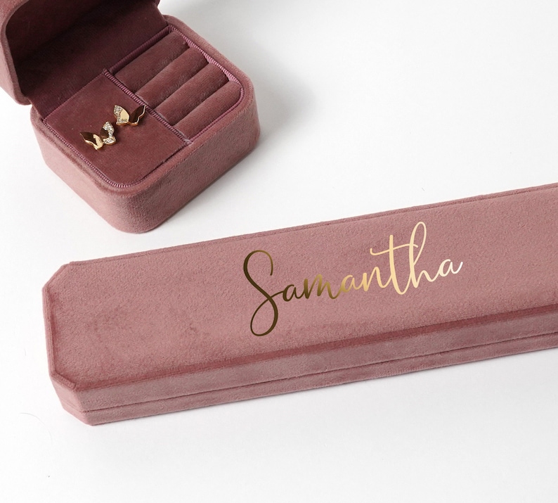 May include: A dusty rose velvet jewelry box with a gold inscription that reads "Samantha".