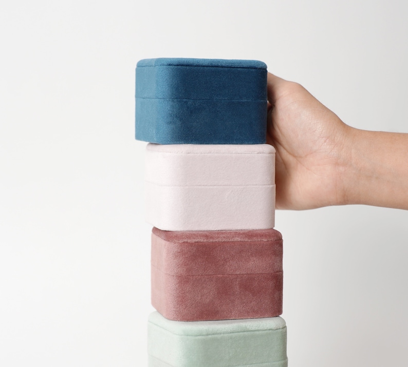 May include: Stack of four velvet jewelry boxes in different colors: teal, light pink, maroon, and light green. The boxes are stacked on top of each other.