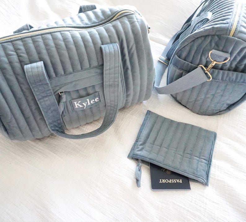 May include: A set of two gray quilted travel bags with gold hardware. The larger bag has a zipper closure and a name tag that reads "Kylee". The smaller bag has a zipper closure and is designed to hold a passport.