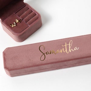 May include: A dusty rose velvet jewelry box with a gold inscription that reads "Samantha".