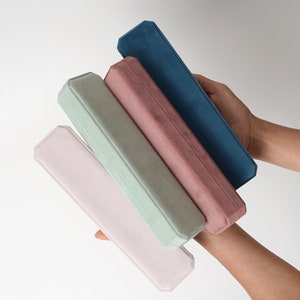 May include: Four velvet-lined boxes stacked on top of each other. The boxes are in shades of pink, green, and blue.