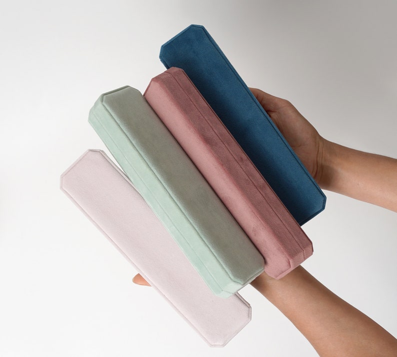 May include: Four velvet-lined boxes stacked on top of each other. The boxes are in shades of pink, green, and blue.