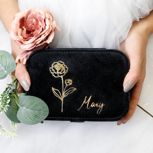 Może przedstawiać: Czarne, aksamitne pudełko na biżuterię z złotym wzorem kwiatowym i wygrawerowanym imieniem "Mary" na przodzie.